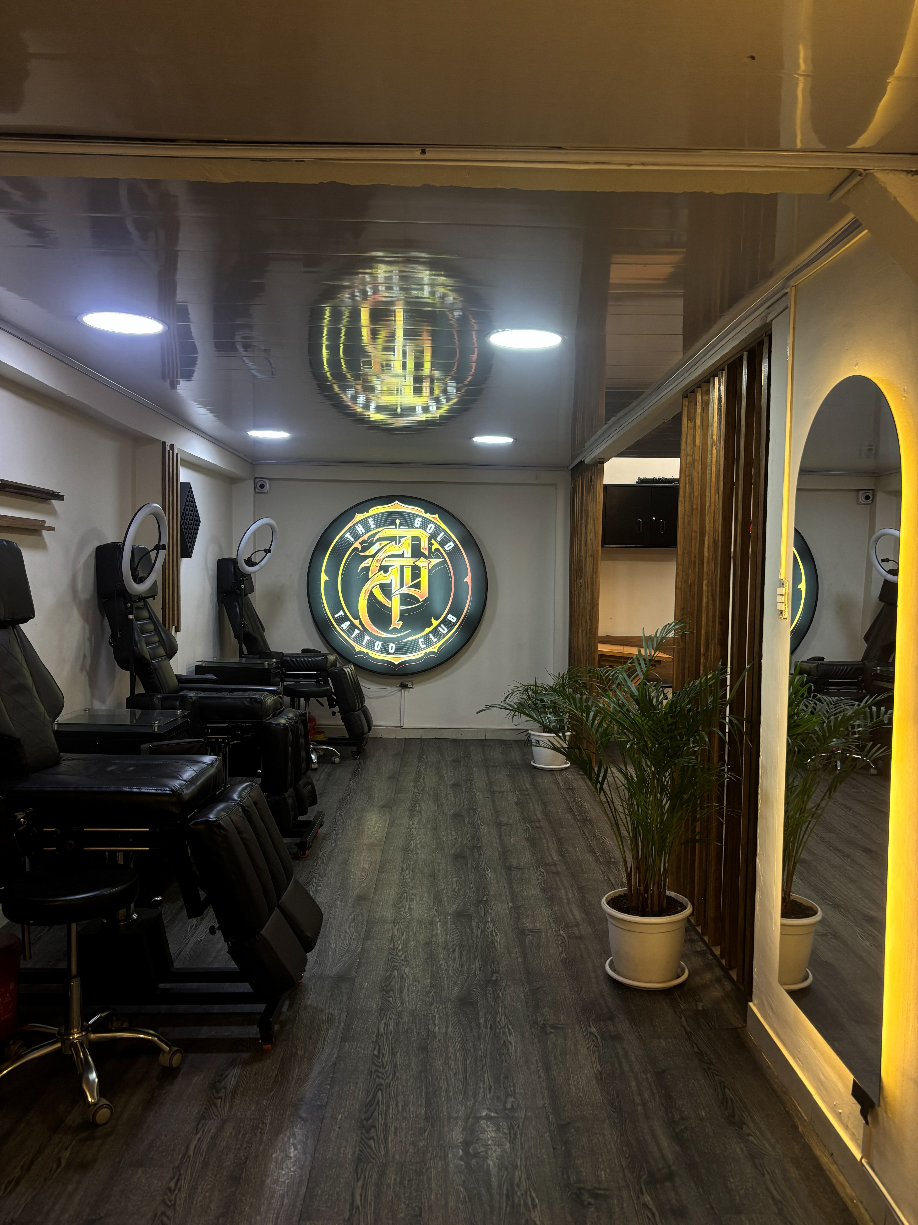Sala del estudio con estaciones de tatuaje, logo de The Gold Tattoo Club y espejo de arco